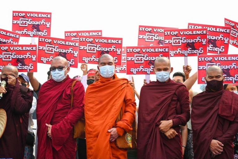 Kelompok Biksu Buddha berdiri di depan pengunjuk rasa memegang tanda selama demonstrasi menentang kudeta militer di Yangon, pada 14 Maret 2021 FOTO: AFP