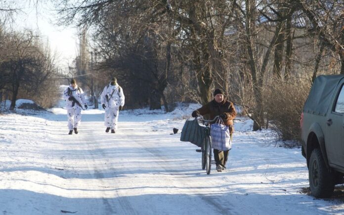 Seorang penduduk setempat berjalan dengan sepedanya ketika anggota angkatan bersenjata Ukraina terlihat di dekat garis pemisah dari pemberontak yang didukung Rusia di luar Horlivka di wilayah Donetsk, Ukraina, 20 Januari 2022. Foto: Reuters.