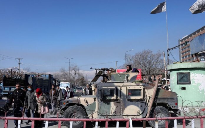 Warga Afghanistan berjalan melewati Humvee dengan seorang pejuang Taliban di atasnya menjaga jalan di Kabul, Afghanistan, 27 Januari 2022. Foto: Reuters.