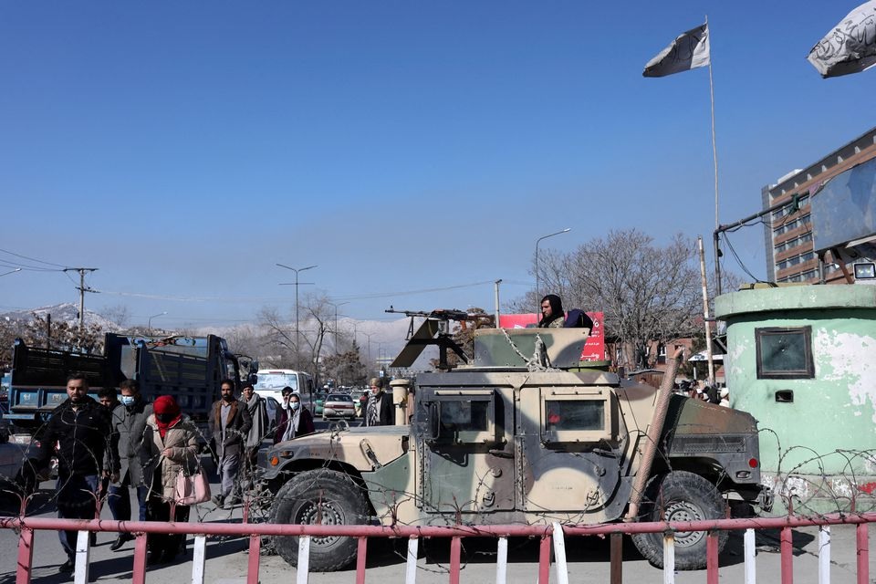 Warga Afghanistan berjalan melewati Humvee dengan seorang pejuang Taliban di atasnya menjaga jalan di Kabul, Afghanistan, 27 Januari 2022. Foto: Reuters.