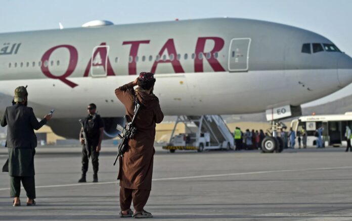 Personel keamanan Qatar (kiri) dan pejuang Taliban berjaga-jaga saat penumpang menaiki pesawat Qatar Airways pada 9 September 2021. Foto: AFP.