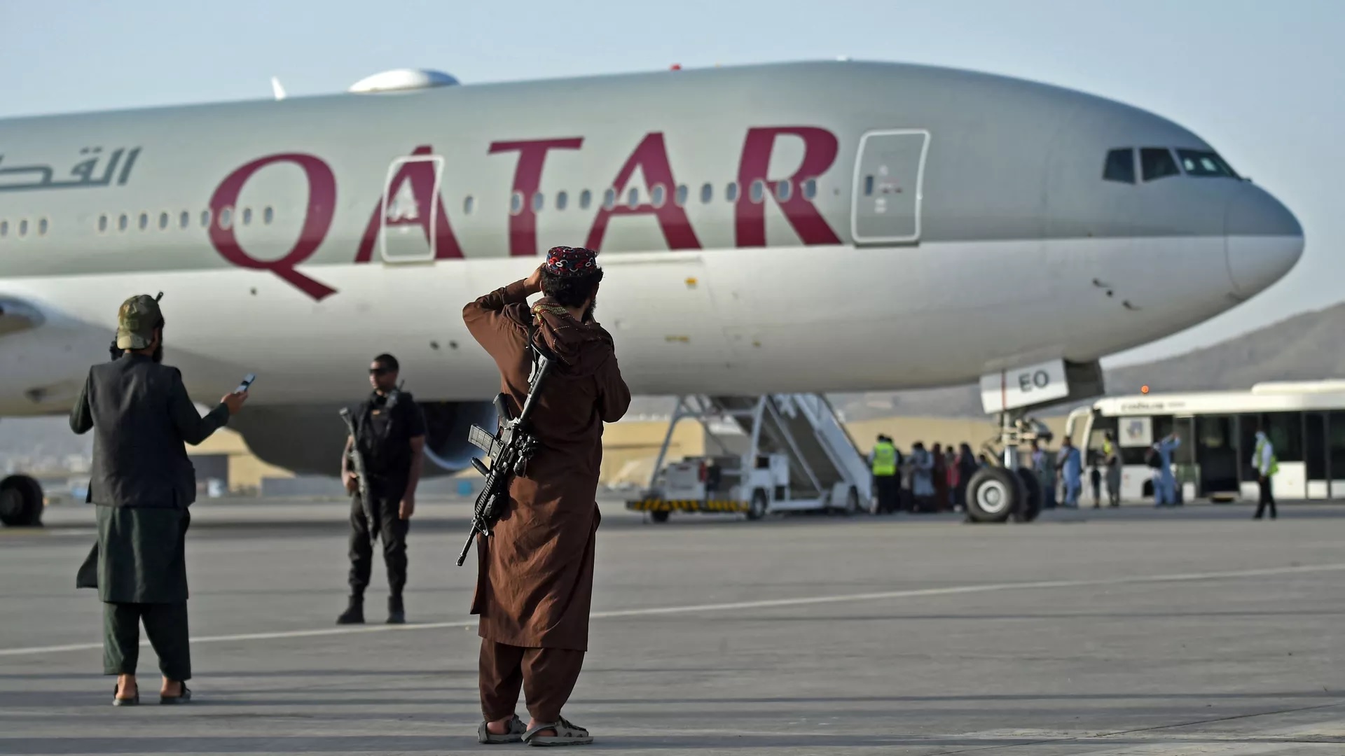 Personel keamanan Qatar (kiri) dan pejuang Taliban berjaga-jaga saat penumpang menaiki pesawat Qatar Airways pada 9 September 2021. Foto: AFP.