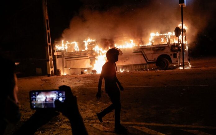 Seseorang warga mengambil foto ketika seorang demonstran berjalan di dekat bus yang dibakar di puncak jalan menuju kediaman Presiden Sri Lanka Gotabaya Rajapaksa selama protes krisis ekonomi ricuh di Kolombo, Sri Lanka 31 Maret 2022. Foto: REUTERS/Dinuka Liyanawatte TPX IMAGES OF THE DAY.