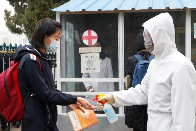 Seorang siswi bertopeng wajah didesinfeksi tangannya oleh seorang pekerja dengan setelan hazmat di pintu masuk sekolah menengah Pyongyang. Foto: Cha Song Ho/AP Photo.