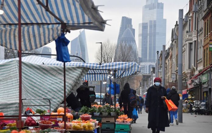 Orang-orang berbelanja di kios-kios pasar, dengan gedung pencakar langit distrik keuangan CIty of London terlihat di belakang, di London, Inggris, 15 Januari 2021. Foto: Reuters/Toby Melville.