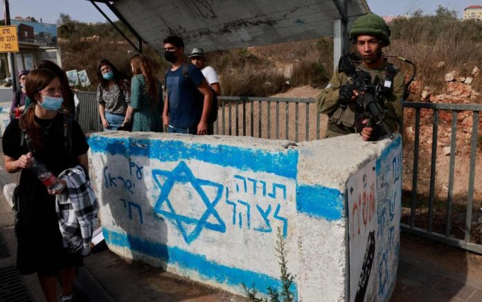 Seorang tentara Israel berjaga di stasiun bus dekat pemukiman Israel Ariel di Tepi Barat yang diduduki, pada 14 Oktober 2021. Foto: AFP.