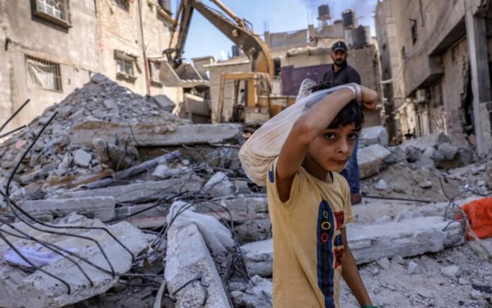 Seorang anak Palestina melihat, ketika para pekerja membersihkan puing-puing sebuah bangunan yang dihancurkan oleh pemboman Israel di Rafah di Jalur Gaza selatan, pada 30 September 2021. Foto: AFP.