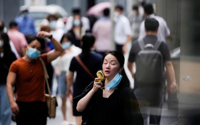 Seorang wanita mengenakan masker wajah menggunakan kipas saat dia berjalan di jalan pada hari yang panas di Shanghai, China 19 Juli 2022. Foto: Reuters/Aly Song.