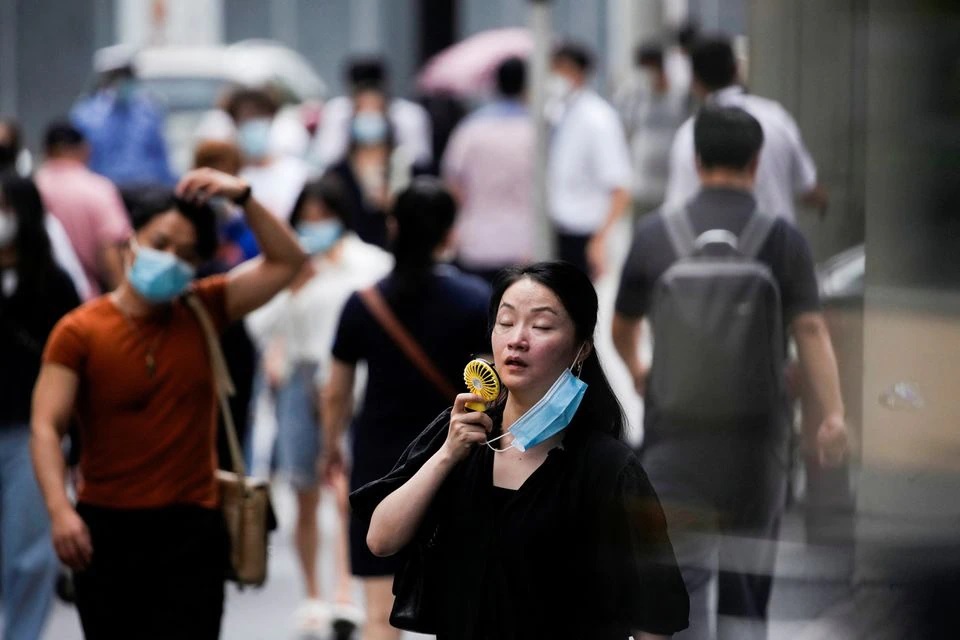 Seorang wanita mengenakan masker wajah menggunakan kipas saat dia berjalan di jalan pada hari yang panas di Shanghai, China 19 Juli 2022. Foto: Reuters/Aly Song.