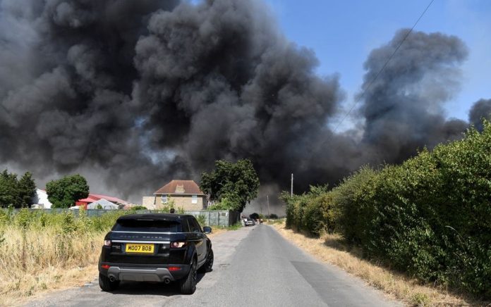 Sebuah mobil melaju di dekat api yang membakar selama gelombang panas, di Rainham, London timur, Inggris, 19 Juli 2022. Foto: Reuters/Tony O'Brien.