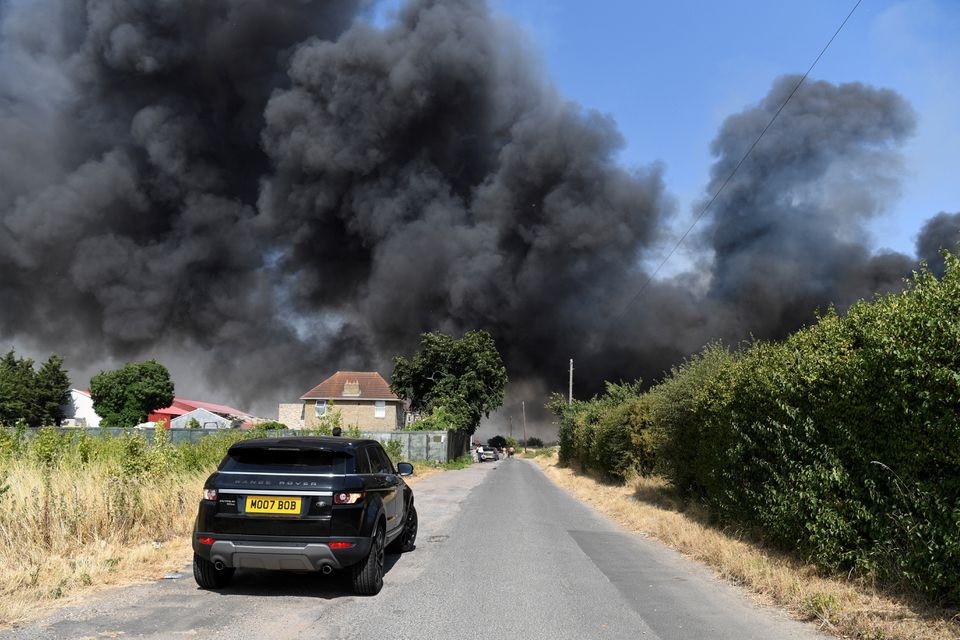 Sebuah mobil melaju di dekat api yang membakar selama gelombang panas, di Rainham, London timur, Inggris, 19 Juli 2022. Foto: Reuters/Tony O'Brien.