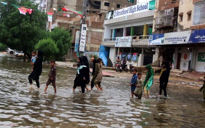 Orang-orang menyeberang jalan yang banjir setelah berhari-hari hujan di Karachi. Foto: Epa.