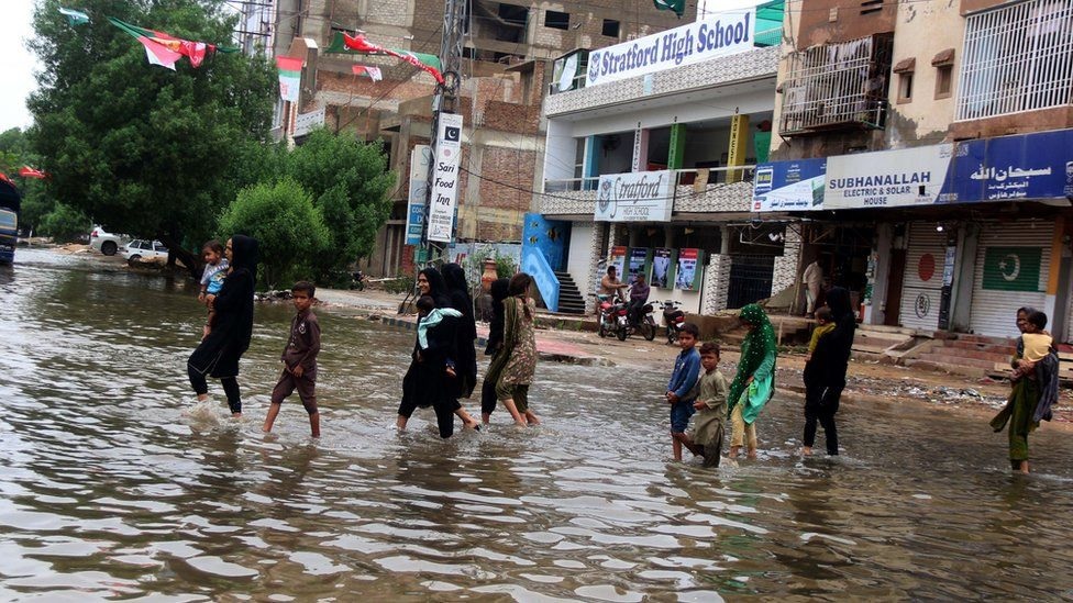 Orang-orang menyeberang jalan yang banjir setelah berhari-hari hujan di Karachi. Foto: Epa.