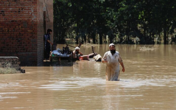 Seorang pria mengarungi banjir mencoba menyelamatkan barang-barangnya setelah hujan dan banjir selama musim hujan di Charsadda, Pakistan 28 Agustus 2022. Foto: Reuters/Fayaz Aziz.