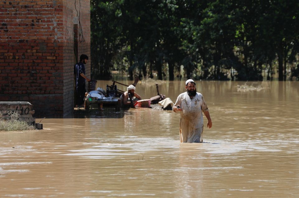 Seorang pria mengarungi banjir mencoba menyelamatkan barang-barangnya setelah hujan dan banjir selama musim hujan di Charsadda, Pakistan 28 Agustus 2022. Foto: Reuters/Fayaz Aziz.