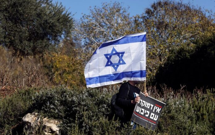 Seorang pria memegang bendera nasional Israel dan tanda yang mengatakan dalam bahasa Ibrani "Tidak ada demokrasi jika ada pendudukan" pada protes di luar Knesset, parlemen Israel, pada hari pemerintahan sayap kanan yang baru dilantik, bersama Benjamin Netanyahu sebagai Perdana Menteri, di Yerusalem 29 Desember 2022. Foto: Reuters/Ammar Awad.