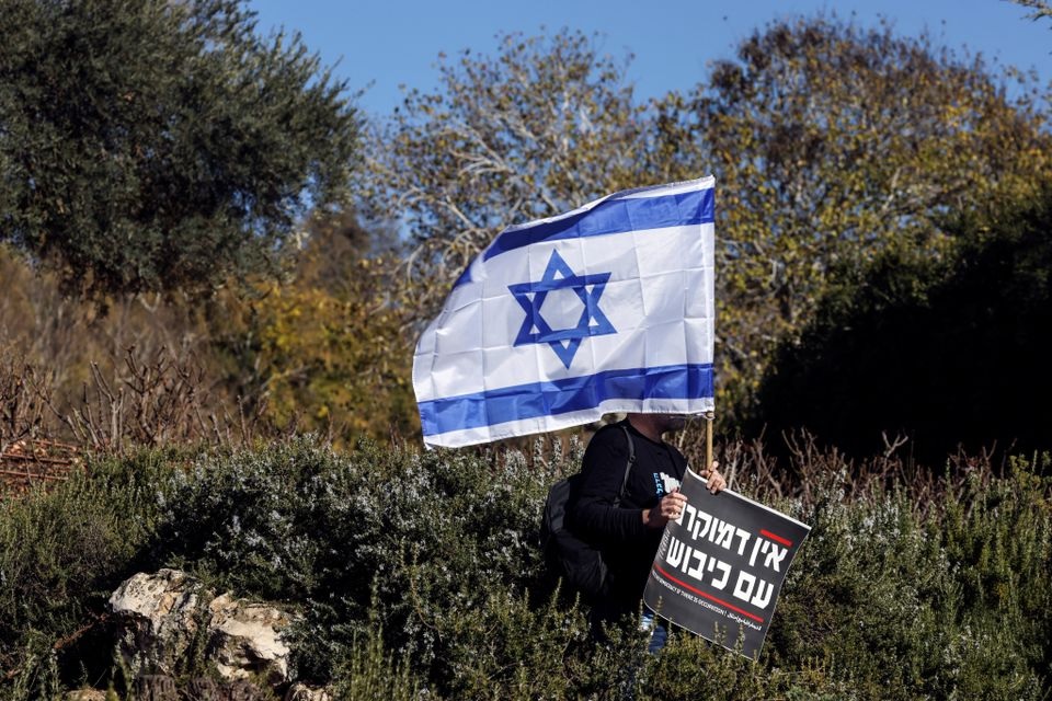 Seorang pria memegang bendera nasional Israel dan tanda yang mengatakan dalam bahasa Ibrani "Tidak ada demokrasi jika ada pendudukan" pada protes di luar Knesset, parlemen Israel, pada hari pemerintahan sayap kanan yang baru dilantik, bersama Benjamin Netanyahu sebagai Perdana Menteri, di Yerusalem 29 Desember 2022. Foto: Reuters/Ammar Awad.