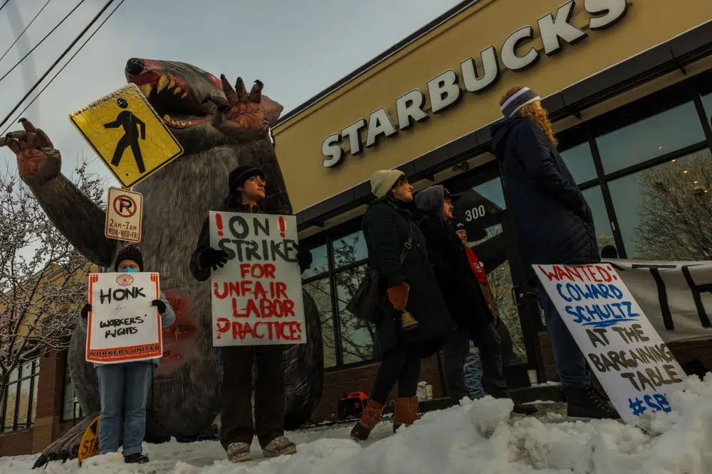 Pekerja Starbucks memegang tanda di depan tikus tiup raksasa selama "Pemogokan Praktik Perburuhan yang Tidak Adil" di St. Paul, Minn. pada Jumat, 16 Desember 2022. Pekerja Starbucks di seluruh AS merencanakan pemogokan tiga hari mulai Jumat. Pemogokan adalah bagian dari upaya mereka untuk menyatukan toko rantai kopi. Foto: Kerem Yücel / Radio Publik Minnesota melalui AP.