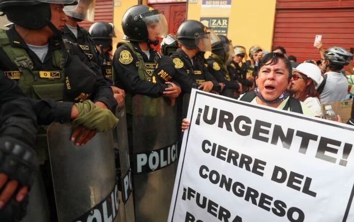 Seorang demonstran memegang tanda bertuliskan "Mendesak! Penutupan Kongres" ketika petugas polisi anti huru hara memegang perisai mereka di tengah protes anti-pemerintah setelah mantan Presiden Peru Pedro Castillo digulingkan, di Lima, Peru 21 Januari 2023. Foto: Reuters/Pilar Olivar.