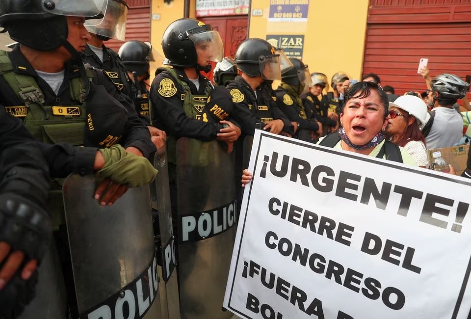 Seorang demonstran memegang tanda bertuliskan "Mendesak! Penutupan Kongres" ketika petugas polisi anti huru hara memegang perisai mereka di tengah protes anti-pemerintah setelah mantan Presiden Peru Pedro Castillo digulingkan, di Lima, Peru 21 Januari 2023. Foto: Reuters/Pilar Olivar.