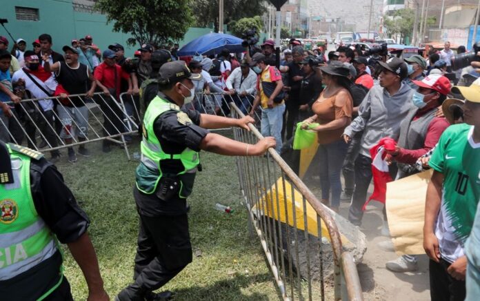 Orang-orang berpegangan pada penghalang di samping seorang petugas polisi ketika para pendukung pemimpin Peru yang digulingkan Pedro Castillo berkumpul di luar penjara polisi tempat dia ditahan, di Lima, 14 Desember 2022. Foto: Reuters/Sebastian Castaneda.