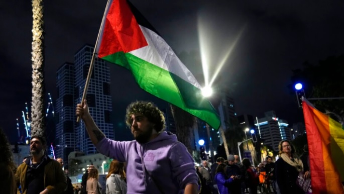 Seorang pengunjuk rasa memegang bendera Palestina di Tel Aviv, Israel, pada demonstrasi menentang pemerintah sayap kanan Perdana Menteri Benjamin Netanyahu, Sabtu, 7 Januari 2023. Foto: AP Photo/ Tsafrir Abayov.