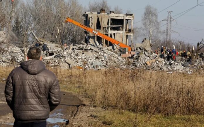 Seorang pria menyaksikan para pekerja memindahkan puing-puing bangunan yang hancur yang diduga merupakan sekolah kejuruan yang digunakan sebagai akomodasi sementara bagi tentara Rusia di Makiivka, Ukraina. Foto: Alexander Ermochenko/Reuters.