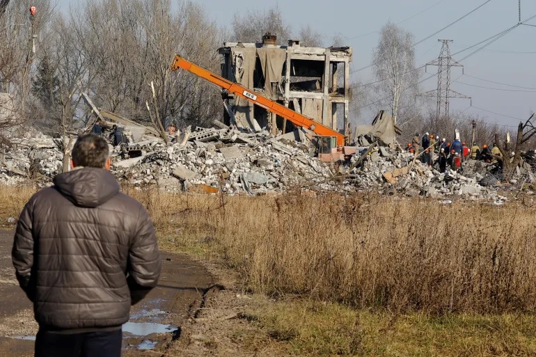 Seorang pria menyaksikan para pekerja memindahkan puing-puing bangunan yang hancur yang diduga merupakan sekolah kejuruan yang digunakan sebagai akomodasi sementara bagi tentara Rusia di Makiivka, Ukraina. Foto: Alexander Ermochenko/Reuters.
