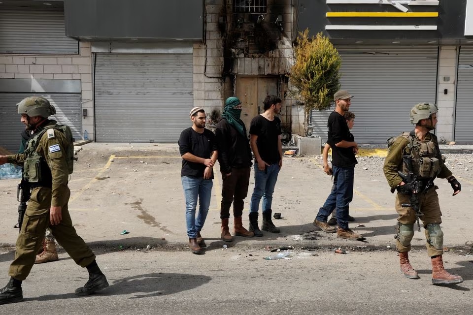 Pemukim Israel berdiri di samping anggota militer Israel, setelah insiden di mana seorang pria bersenjata Palestina membunuh dua pemukim Israel, di dekat Hawara di Tepi Barat yang diduduki Israel, 27 Februari 2023. Foto: Reuters/Ammar Awad.