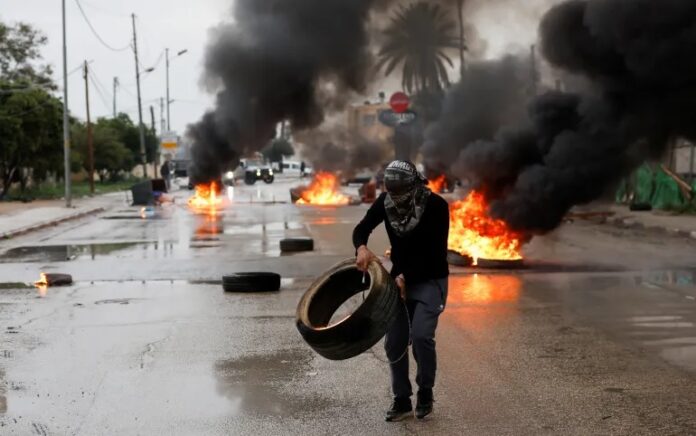 Seorang pria Palestina membawa ban untuk memblokir pasukan Israel menjelang serangan militer di Jericho. Foto: Mohammed Torokman/Reuters.