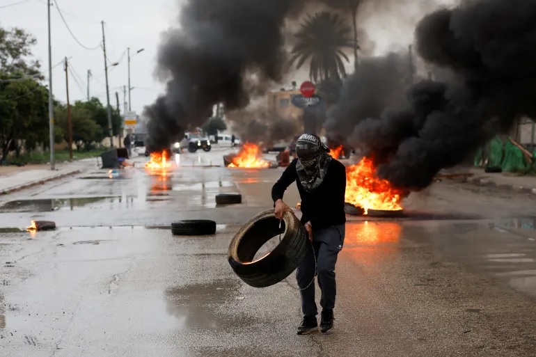 Seorang pria Palestina membawa ban untuk memblokir pasukan Israel menjelang serangan militer di Jericho. Foto: Mohammed Torokman/Reuters.