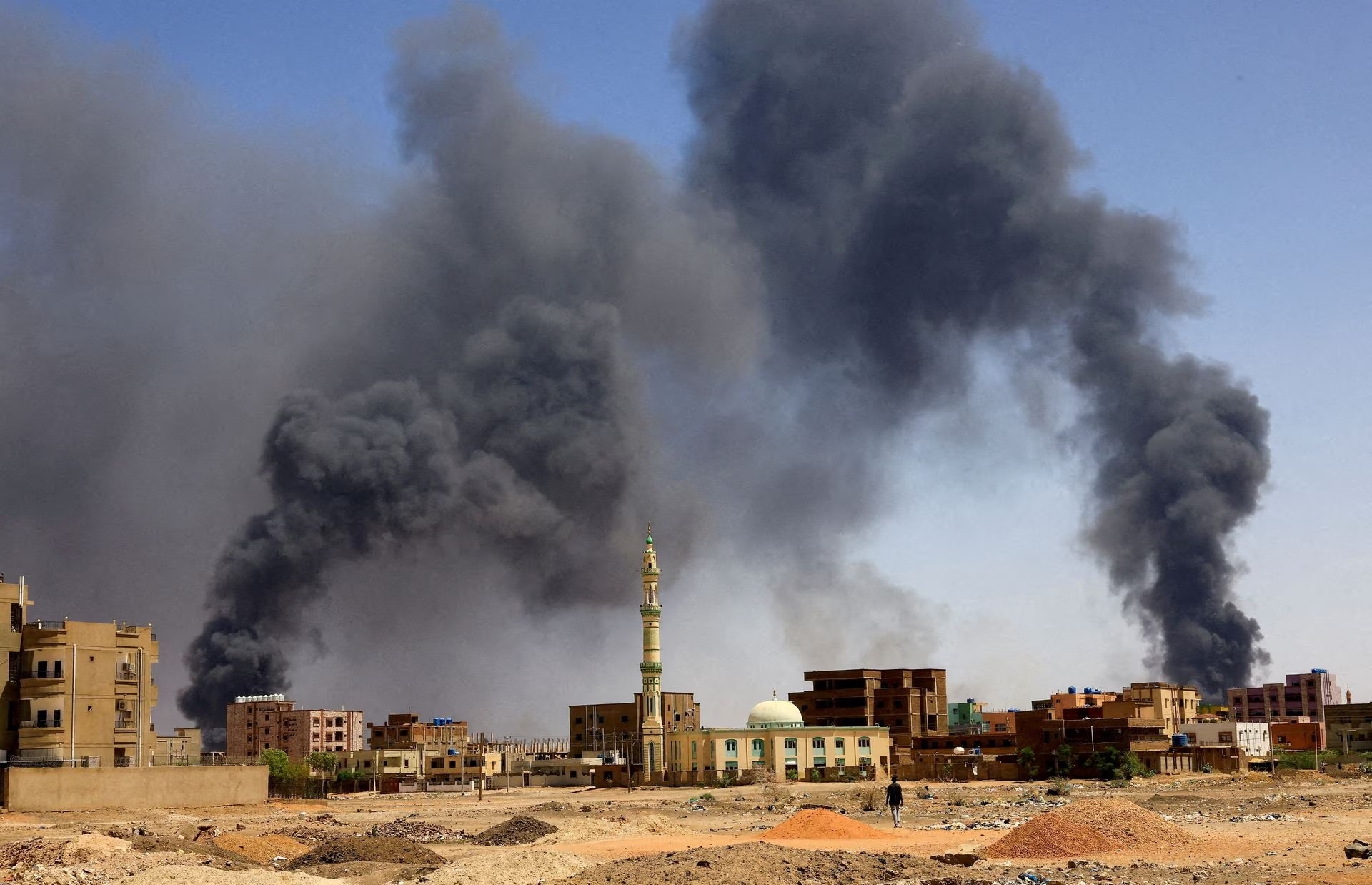 Seorang pria berjalan sementara asap mengepul di atas bangunan setelah pengeboman udara, selama bentrokan antara Pasukan Dukungan Cepat paramiliter dan tentara di Khartoum Utara, Sudan, 1 Mei 2023. Foto: Reuters/Mohamed Nureldin Abdallah.