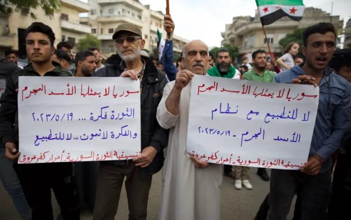 Para pengunjuk rasa memegang spanduk bertuliskan: 'Suriah tidak diwakili oleh penjahat al-Assad' dan 'Tidak untuk normalisasi dengan rezim' di Idlib yang dikuasai pemberontak. Foto: Ali Haj Suleiman/Al Jazeera.