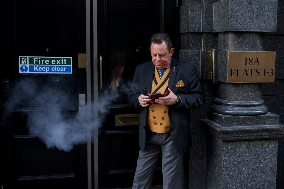 Seorang pria merokok rokok elektrik di pintu darurat kebakaran di London, Inggris, 13 November 2022. Foto: Reuters/Kevin Coombs.