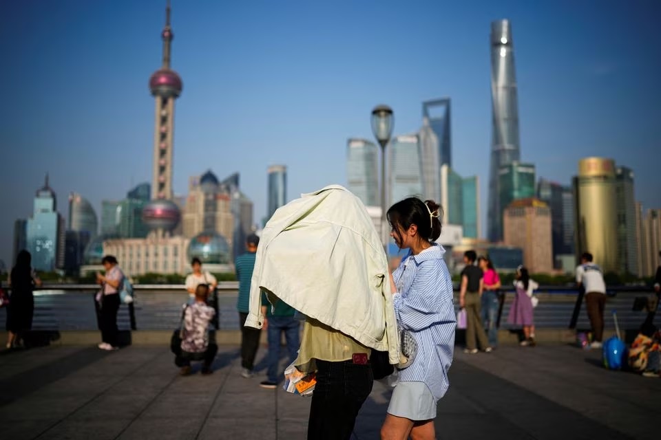 Seseorang menggunakan pakaian untuk melindungi diri dari sinar matahari, saat mereka berjalan di atas Bund pada hari yang panas, di Shanghai, China, 15 Mei 2023. Foto: Reuters/Aly Song/File Foto.