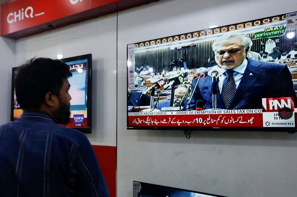 Seorang salesman melihat ke layar televisi yang memperlihatkan Menteri Keuangan Pakistan Ishaq Dar sedang mempresentasikan anggaran untuk tahun fiskal 2023/24 di parlemen di Islamabad, di sebuah toko di Karachi, Pakistan, 9 Juni 2023. Foto: Reuters/Akhtar Soomro.