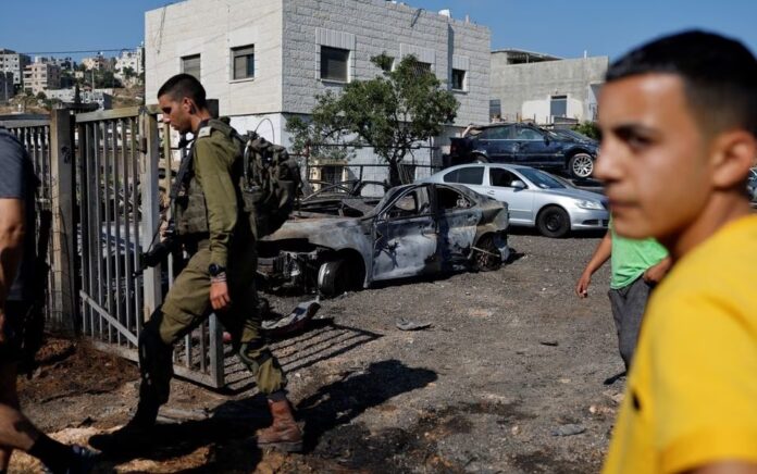 Seorang pria Palestina memeriksa kendaraan yang terbakar setelah serangan pemukim Israel di dekat Ramallah di Tepi Barat yang diduduki Israel, 21 Juni 2023. Foto: Reuters/Ammar Awad.