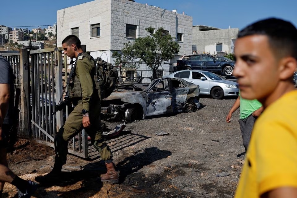 Seorang pria Palestina memeriksa kendaraan yang terbakar setelah serangan pemukim Israel di dekat Ramallah di Tepi Barat yang diduduki Israel, 21 Juni 2023. Foto: Reuters/Ammar Awad.
