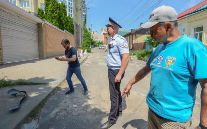 Seorang petugas polisi berjaga-jaga ketika wartawan merekam di dekat blok apartemen bertingkat yang rusak menyusul laporan serangan pesawat tak berawak di Voronezh, Rusia 9 Juni 2023. Foto: Reuters/Vladimir Lavrov.