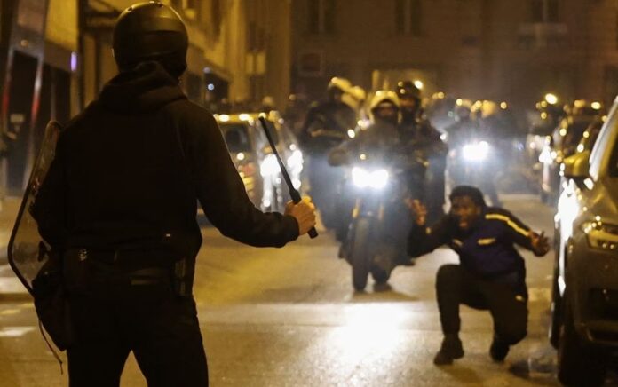 Seseorang bereaksi ketika seorang petugas polisi memegang tongkat selama protes setelah kematian Nahel, seorang remaja berusia 17 tahun yang dibunuh oleh seorang petugas polisi Prancis di Nanterre selama pemberhentian lalu lintas, di Paris, Prancis, 2 Juli 2023. Foto: Reuters/Nacho Doce.