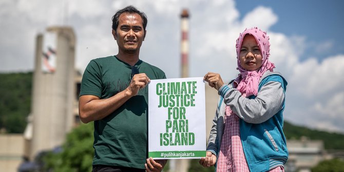 Warga Pulau Pari, Edi (kiri) dan Asmania berfoto dengan membawa poster 'Keadilan Iklim untuk Pulau Pari' di depan pabrik semen Holcim di Eclepens, Swiss, pada 11 Juni 2023. Edi dan Asmania jauh-jauh mendatangi produsen semen raksasa Swiss untuk melakukan protes (Foto: AFP)